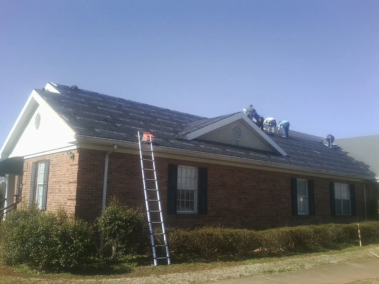 Crew tearing shingles off a brick ranch roof with a ladder set — Emergency Roof Repair work by our crew in Arden