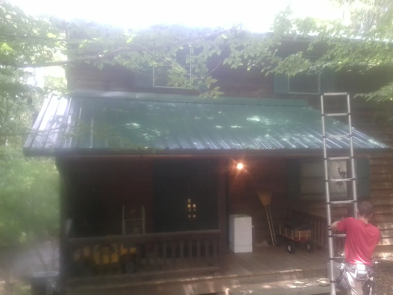 Worker on a ladder at the green porch roof of a wooded cabin in Arden